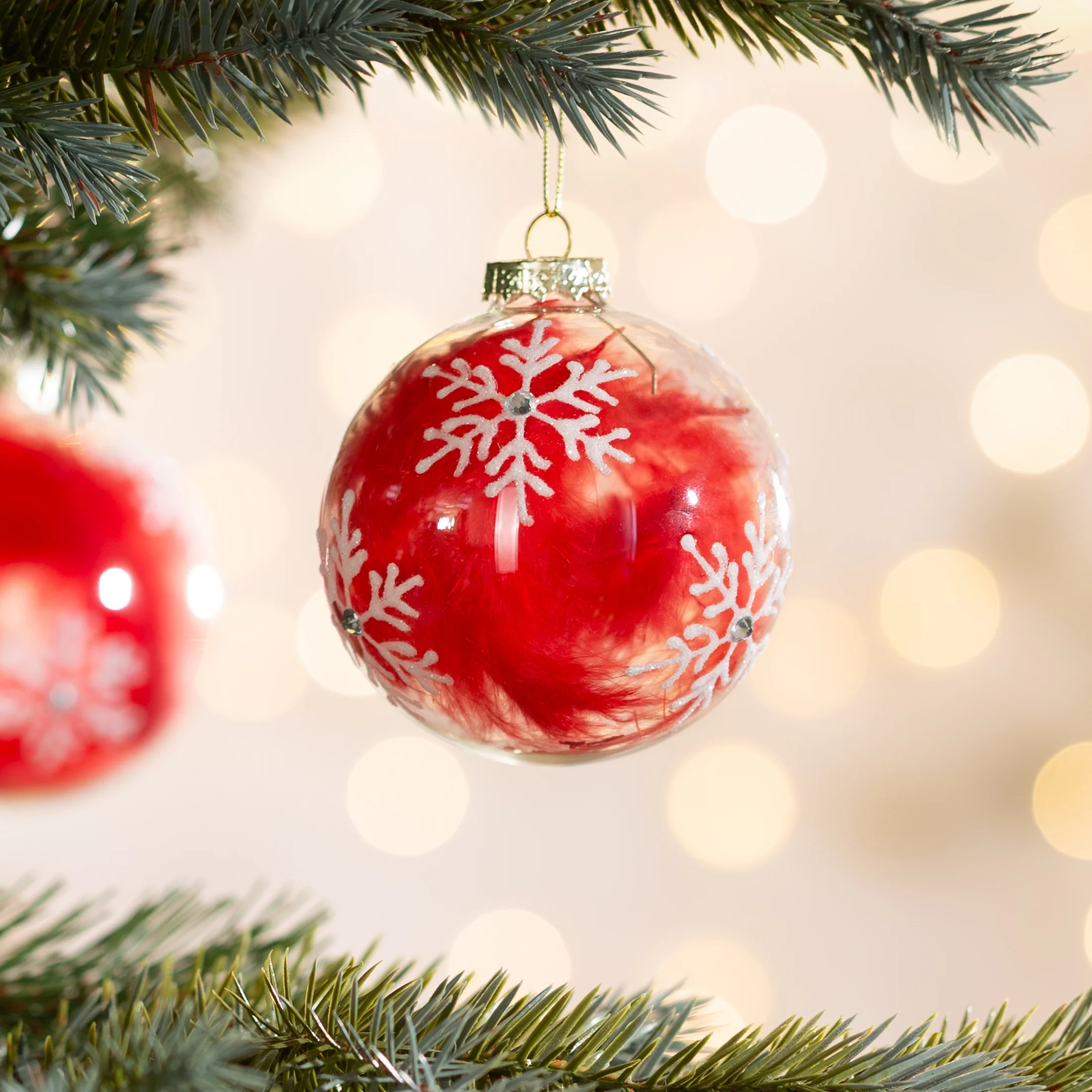 Bombka z transparentnego szkła zdobiona aplikacją ze śnieżynkami i wypełniona czerwonym puchem | eurofirany